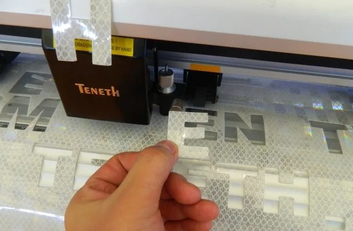 Machine de découpe en action, avec l'opérateur retirant la lettre 'E' du design.