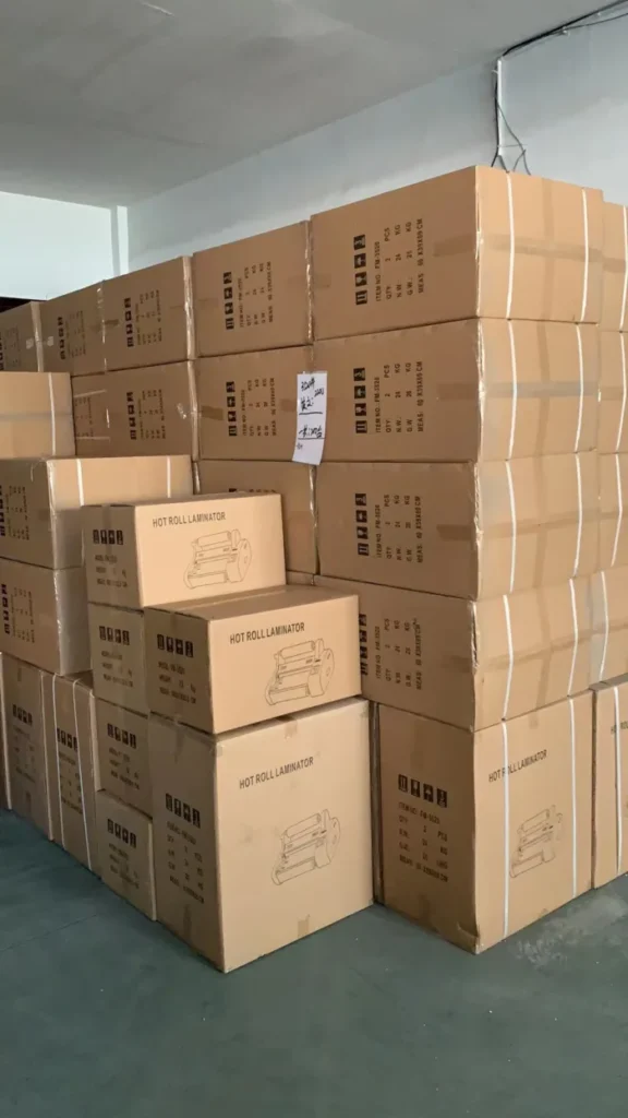 Cartons de plastifieuses empilés dans un entrepôt, étiquetés "HOT ROLL LAMINATOR"